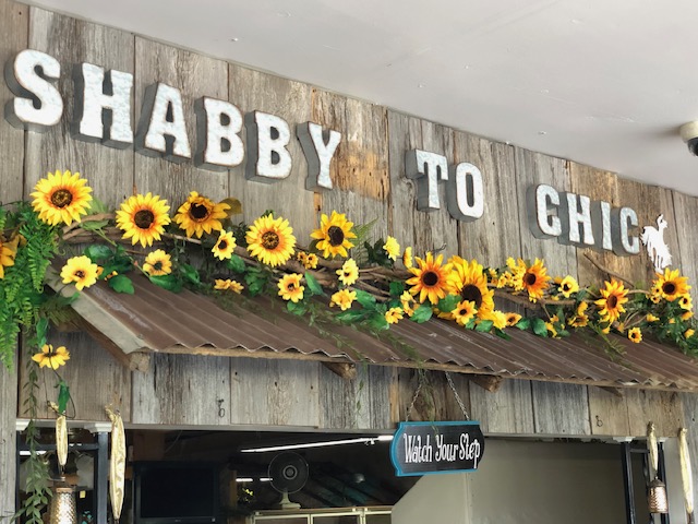 image displays a prominent sign reading "SHABBY TO CHIC" and features a decorative arrangement of sunflowers and greenery on a rustic wooden background